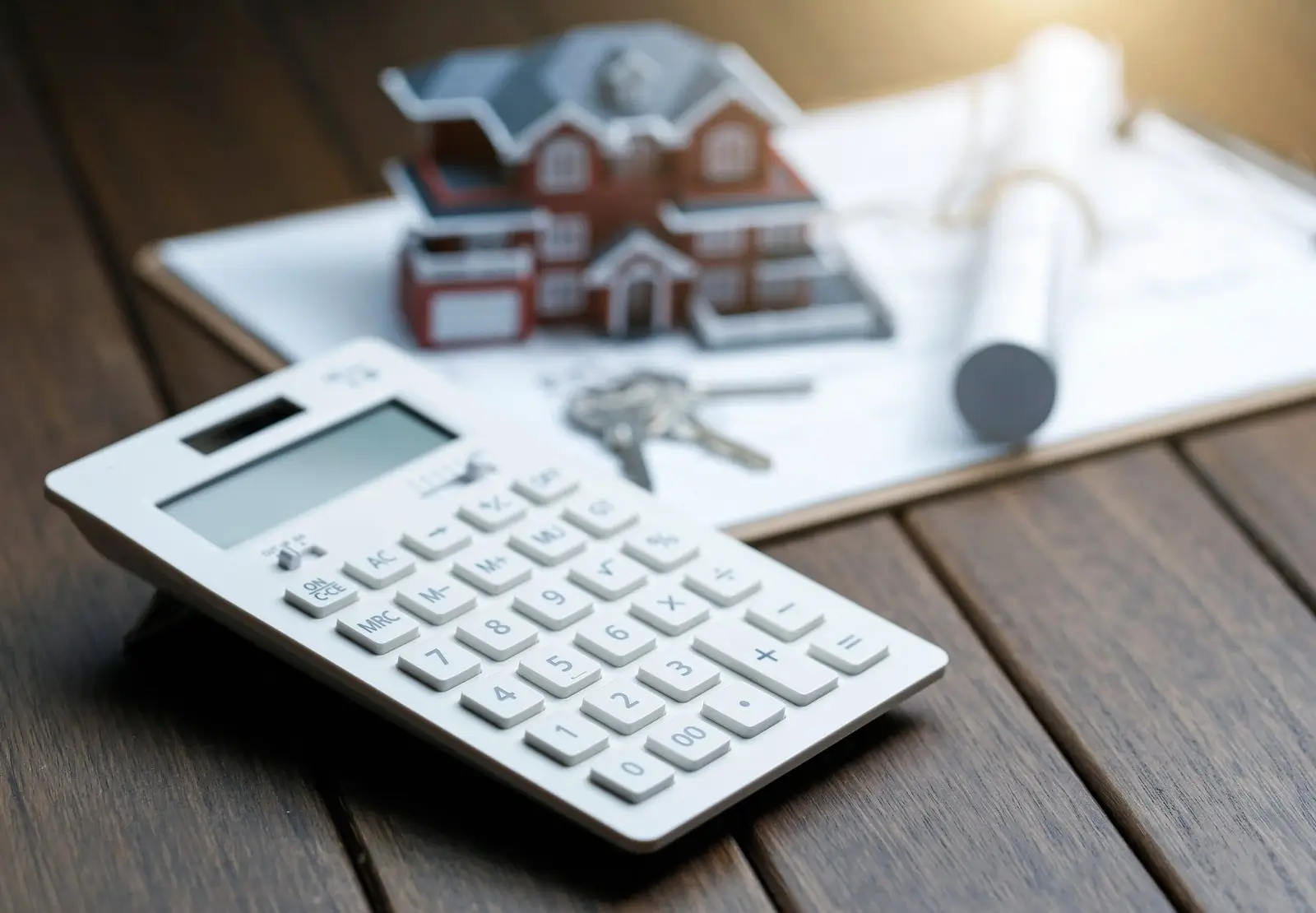 Calculadora junto a una maqueta de vivienda, llaves y planos, representando el cálculo fiscal de la exención por reinversión en vivienda habitual en el IRPF.